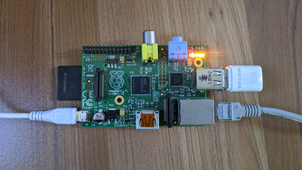 Raspberry Pi Model B acting as a WiFi router. White cable on the left is power. USB WiFi dongle on the top right. Ethernet cable from internet service provider on the bottom left.